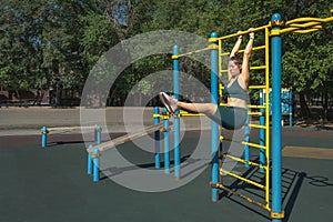 Young woman pumps her abdominal muscles on a metal Swedish wall on a street sports ground.