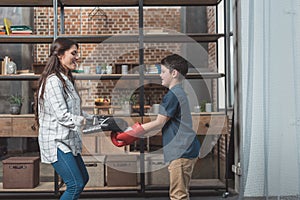 Young woman with punching pads on hands and her little son in boxing gloves making a