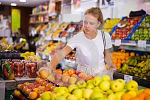 Young woman purchaser choosing apples in grocery