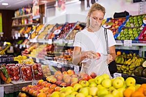 Young woman purchaser choosing apples in grocery