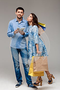 Young woman with purchases, man holding money over grey background.