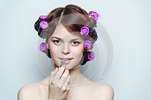 young woman with purple curlers on her head naked shoulders gray background