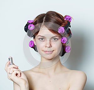 young woman with purple curlers on her head naked shoulders gray background