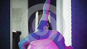Young woman in purple sports suit doing fitness - doing exercises with fitness ball in neon lighting
