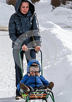 A young woman pushing her little son sitting in the sledge. Winter entertainment.
