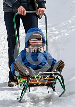 A young woman pushing her little son sitting in the sledge. Winter entertainment.