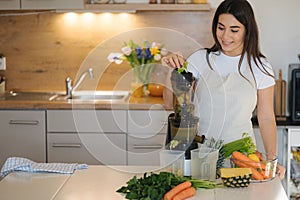 Young woman put celery into juicer. Process of making healthy drink. Place for text