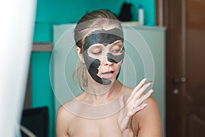 A young woman puts a black mask on her face and looks at her hand in the mud in surprise. Beauty photo of a woman with a black mas