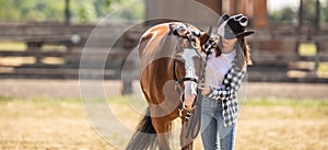 Young woman puts a bridle on horse& x27;s head outdoors