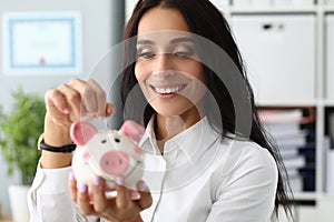 Young woman puts coins in ceramic piggy bank