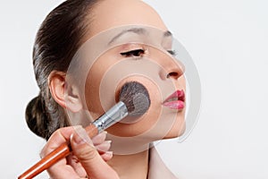 A young woman puts makeup on her face with a brush. on white background