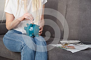 Young woman putting 10 euro into money box sitting on sofa at home