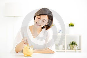 Young Woman Putting Coin In Piggy Bank