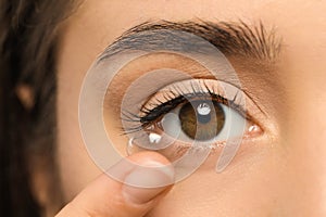 Young woman putting contact lens in her eye, closeup