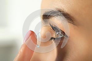 Young woman putting contact lens in her eye, closeup