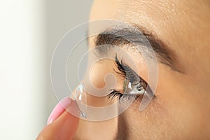 Young woman putting contact lens in her eye, closeup