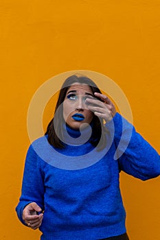 Young woman putting contact lens in her eye on vertical orange background