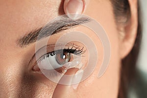 Young woman putting contact lens in her eye