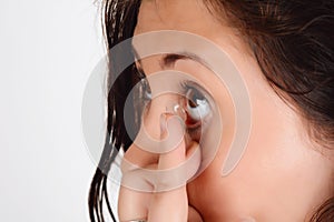 Young woman putting contact lens in her right eye, close up