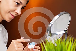 A young woman is putting on contact lenses in front of the mirror.