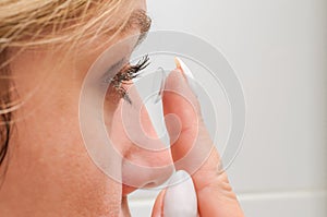 Young woman putting on contact lenses for vision correction