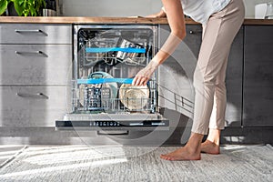 Young woman putting dirty ceramic dish in the dishwasher. Household and helpful technology concept