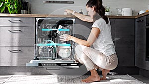 Young woman putting dirty ceramic dish in dishwasher. Household and helpful technology concept