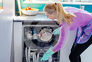 Young woman putting dirty dishes to dishwasher