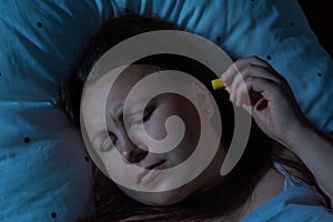 Young woman putting earplugs into her ears for the noise reduction before sleep, insomnia