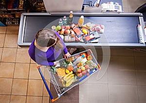 Young woman putting goods from shopping cart on counter for checkout