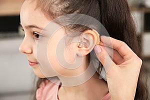 Young woman putting hearing aid in daughter`s ear indoors