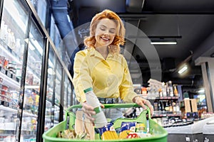 Young woman putting milk bottle in shop cart, choosing dairy products in supermarket, female buyer buying essentials on