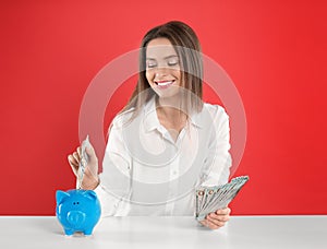 Young woman putting money into piggy bank at table on background