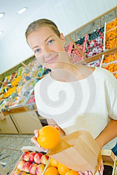 Young woman putting orange in paper bag