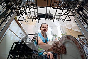 A young woman putting a plate in the dishwasher. Inside view of a dishwasher. Washing dirty dishes at home, home chores concept