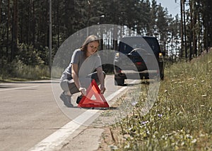 Young woman putting red triangle caution sign on road near broken car on roadside