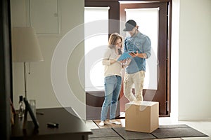 Young woman putting signature receiving parcel from courier at h