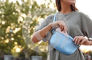 Young woman putting smartphone in stylish bum bag outdoors, closeup