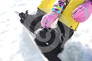 Young woman putting on snowboard outdoors, closeup. Winter vacation