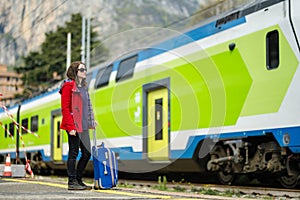 Young woman on a railway station. A girl waiting for a train on a platform. Female tourist with a luggage suitcase ready to travel