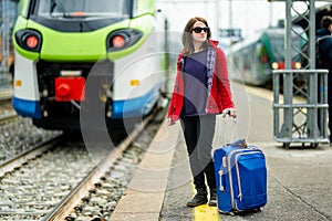 Young woman on a railway station. A girl waiting for a train on a platform. Female tourist with a luggage suitcase ready to travel