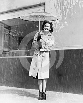 Young woman in a raincoat and umbrella standing in the rain