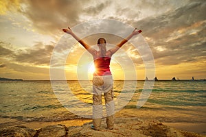 Young woman with raised hands standing on shore and looking to a