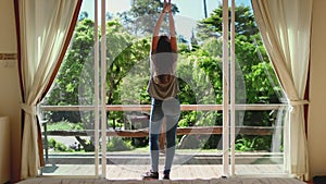 Young woman raises hands up, down in luxury hotel room. Beautiful girl stands on balcony in sunshine