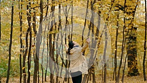 A young woman raises her arms and spins around as the autumn leaves fall.