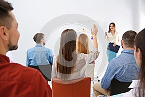 Young woman raising hand to ask question at business training, back view