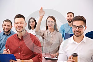Young woman raising hand to ask question at business training on background