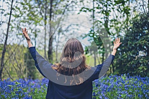 Young woman raising her arms in bluebell meadow