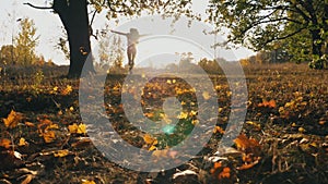 Young woman raising her hands and enjoying falling autumn leaves. Happy girl showing joyful emotions with sunset at