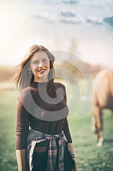 Young woman on ranch with horse who graze in the background